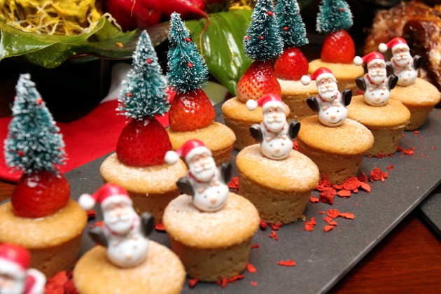 A colourful assortment of cupcakes decorated with mini Santa Claus and pine trees.