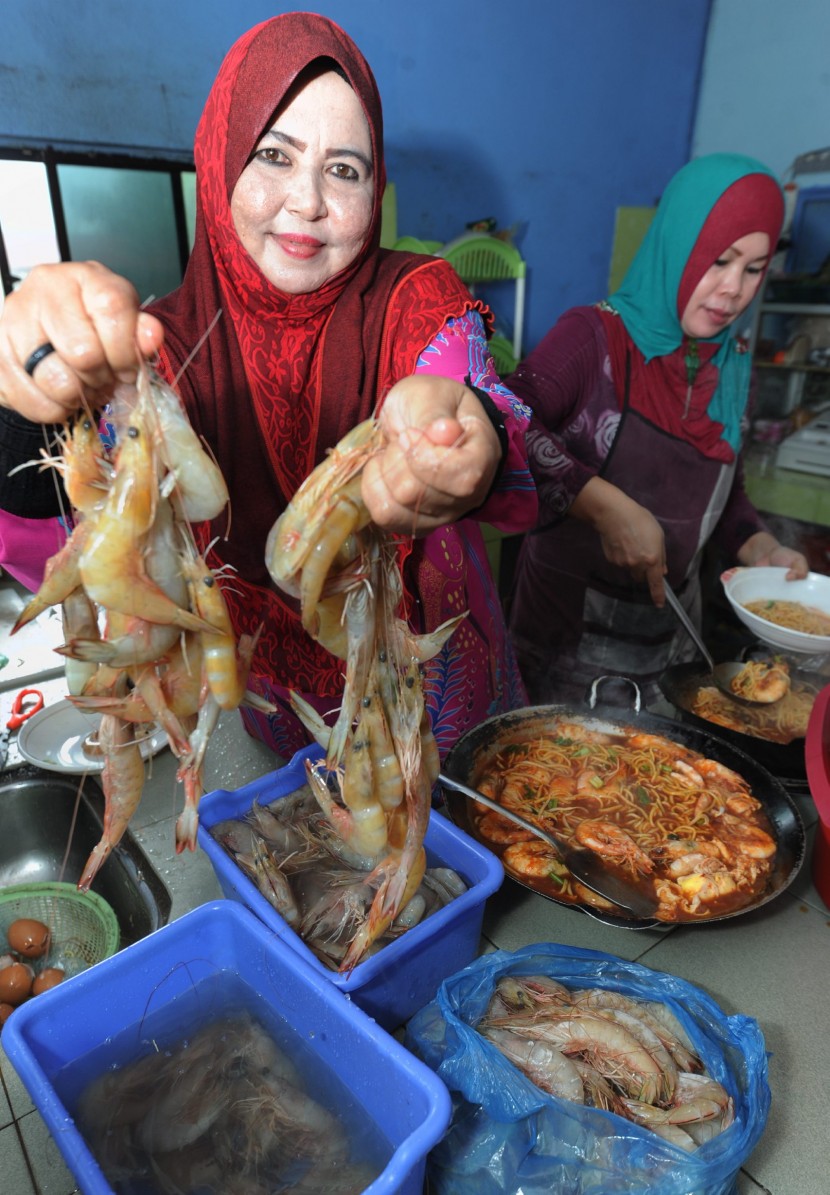Mee Udang Kak Ju's Julia Ahmad showing off the big prawns her village's fishermen supply to her while her assistant Yani Manan, ladles steaming bowls of prawn noodles for waiting customers.